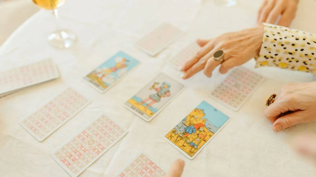 Pessoas participando de uma consulta de tarot com cartas abertas e viradas sobre uma mesa clara.