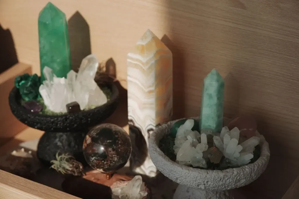 Altar com pontas de cristais verdes, quartzos brancos, torre de pedra e esfera decorativa iluminados pela luz natural.