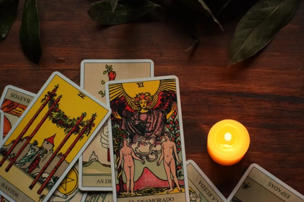 Carta de tarot Os Enamorados em destaque, cercada por outras cartas e uma vela acesa sobre mesa de madeira.
