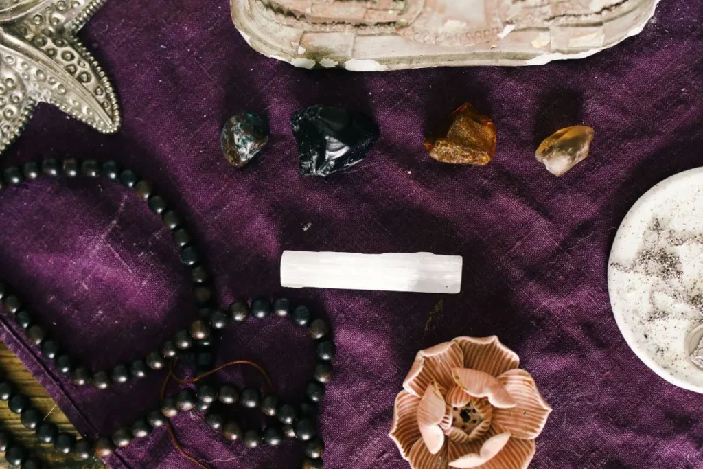Cristais e pedras naturais organizados sobre tecido roxo com contas, enfeites e objetos espirituais.