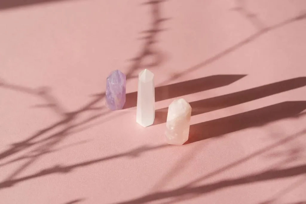 Três cristais lapidados em tons de lilás, branco e rosa sobre fundo rosa iluminado pelo sol.