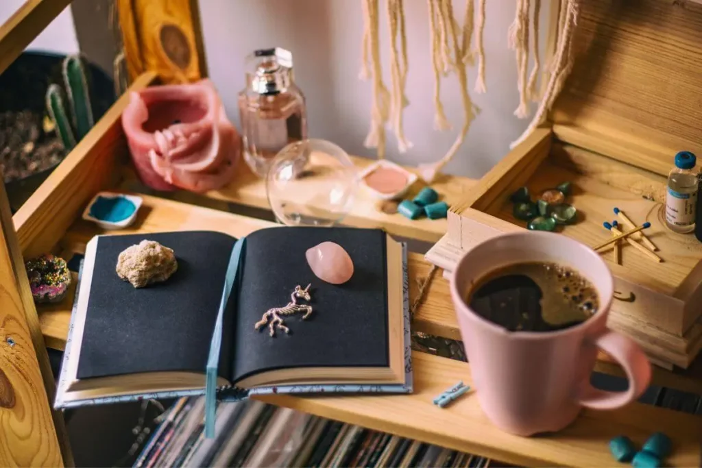 Diário aberto com cristais, pingente e uma caneca de café sobre mesa de madeira.