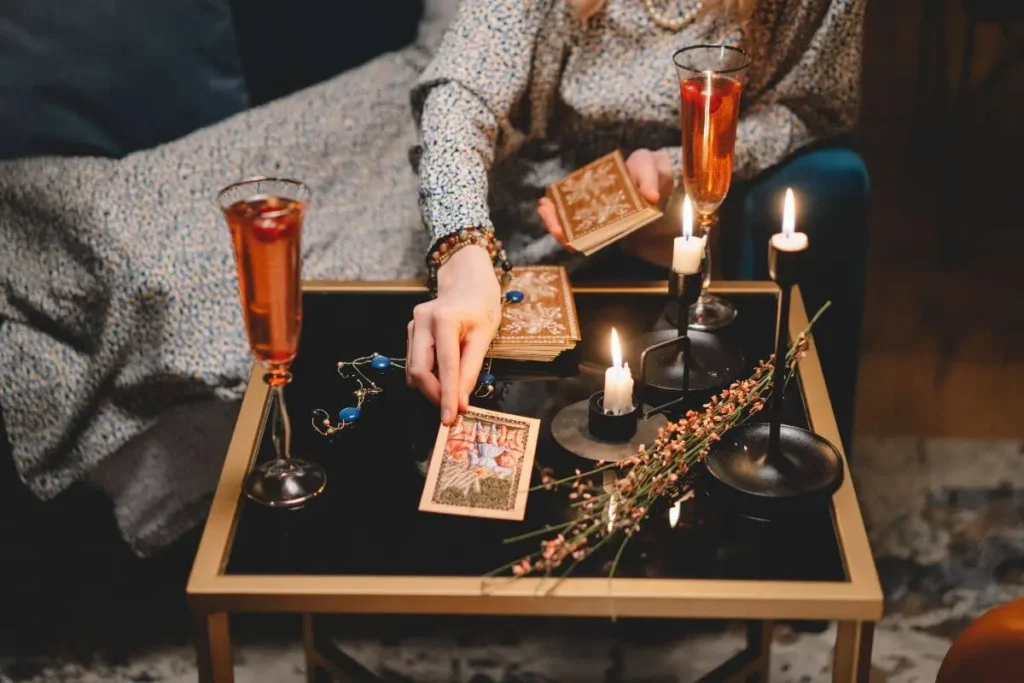 Pessoa realizando uma leitura de tarot sobre uma mesa com cartas, velas acesas, taças e elementos decorativos.
