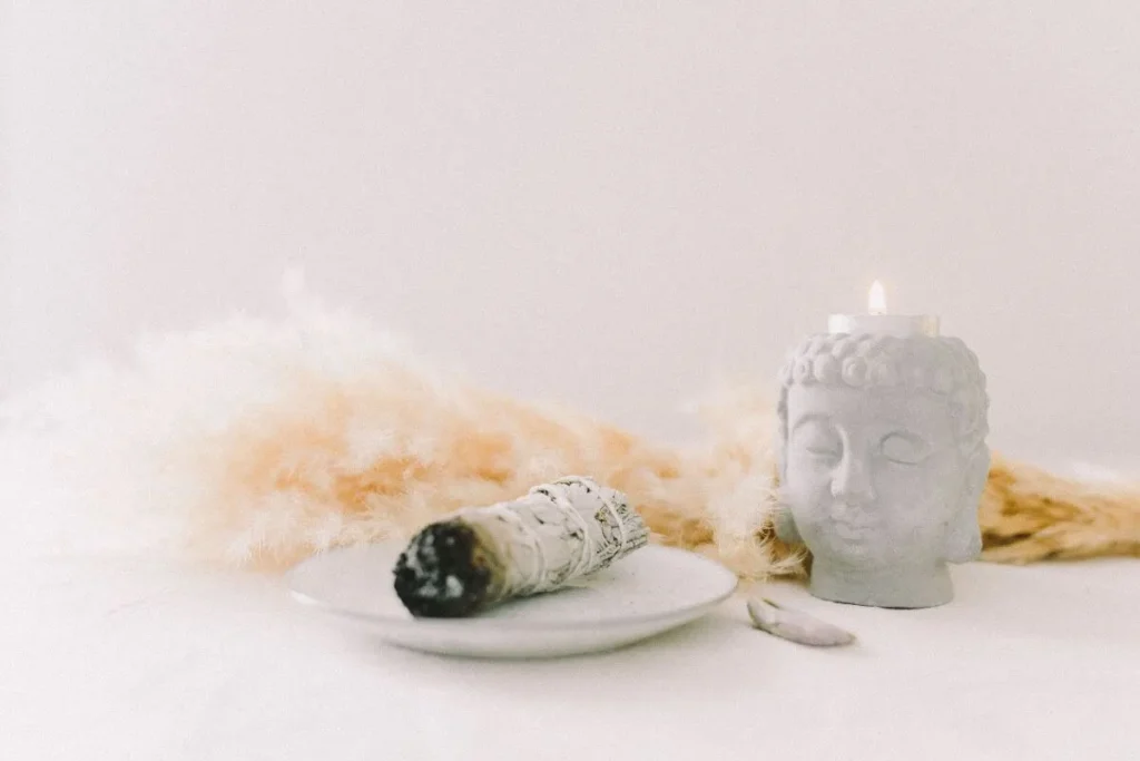 Sálvia branca queimada ao lado de vela decorativa em formato de Buda para limpeza energética.