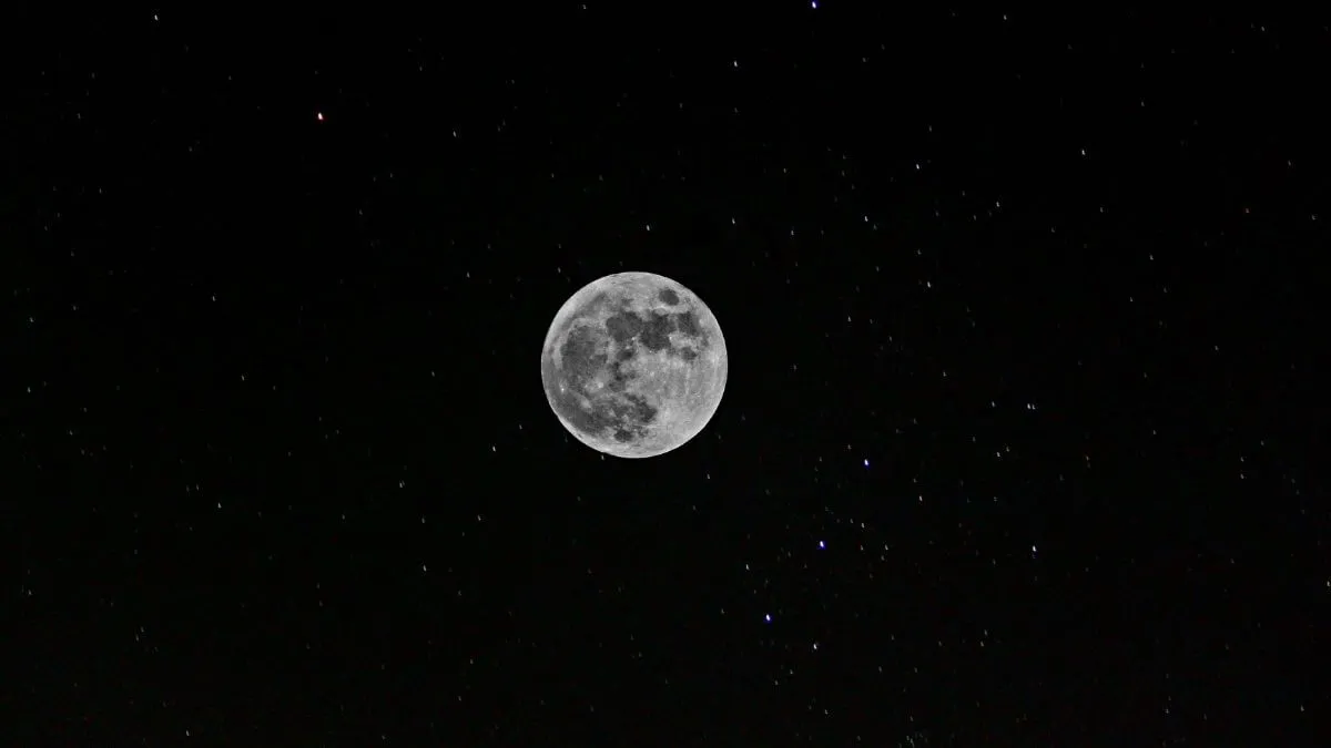 Lua cheia iluminada no centro de um céu noturno escuro e repleto de estrelas.