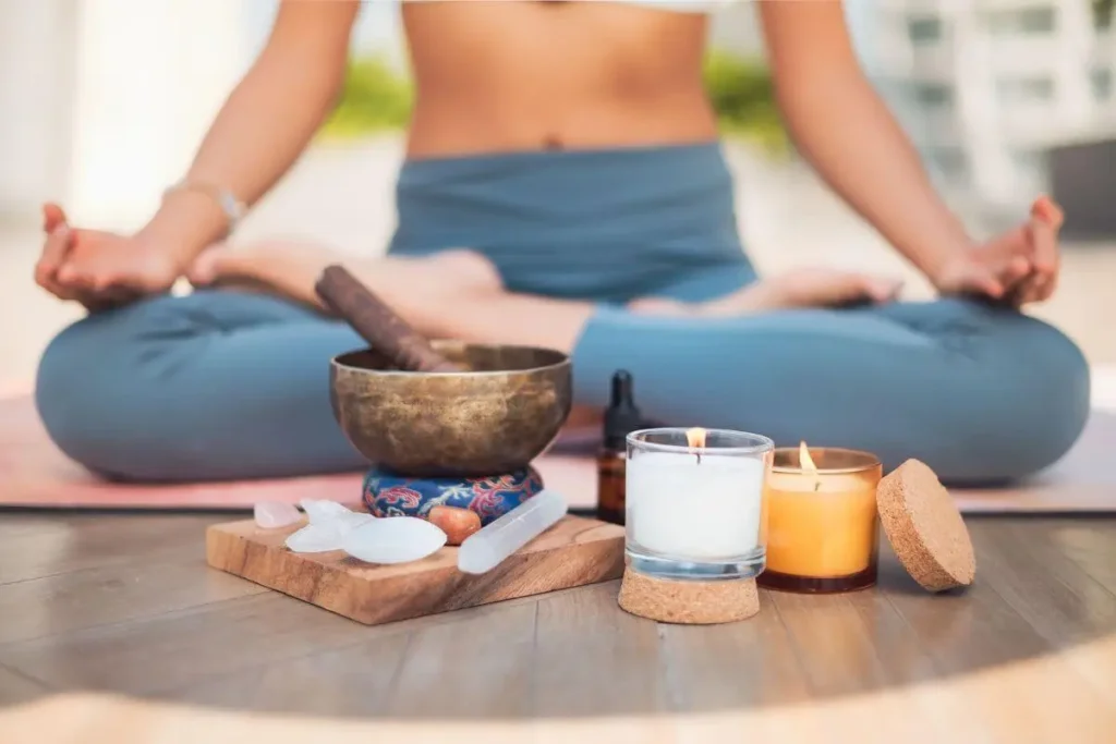 Pessoa meditando em posição de lótus com velas acesas, cristais e tigela tibetana, criando um ambiente de paz, equilíbrio, manifestação e conexão espiritual.