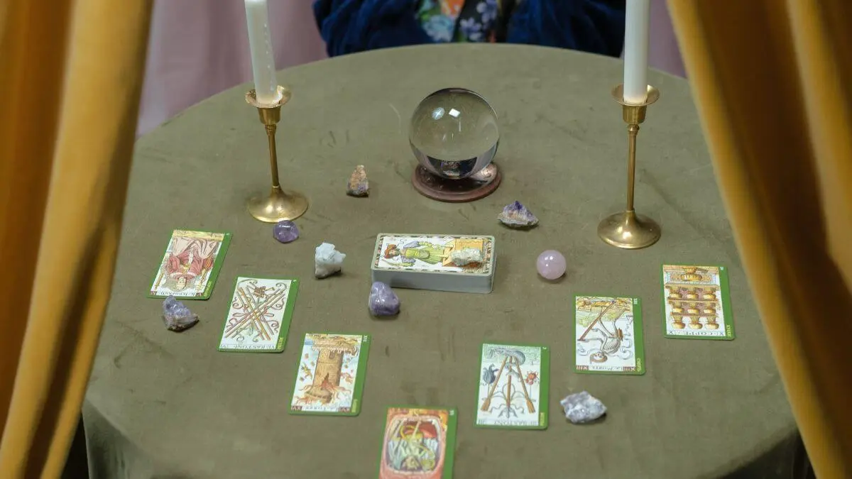 Mesa de leitura de tarot com cartas, cristais, velas e bola de cristal.