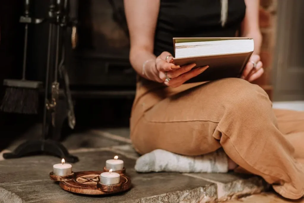 Mulher sentada com um livro nas mãos ao lado de velas acesas em um ambiente acolhedor.