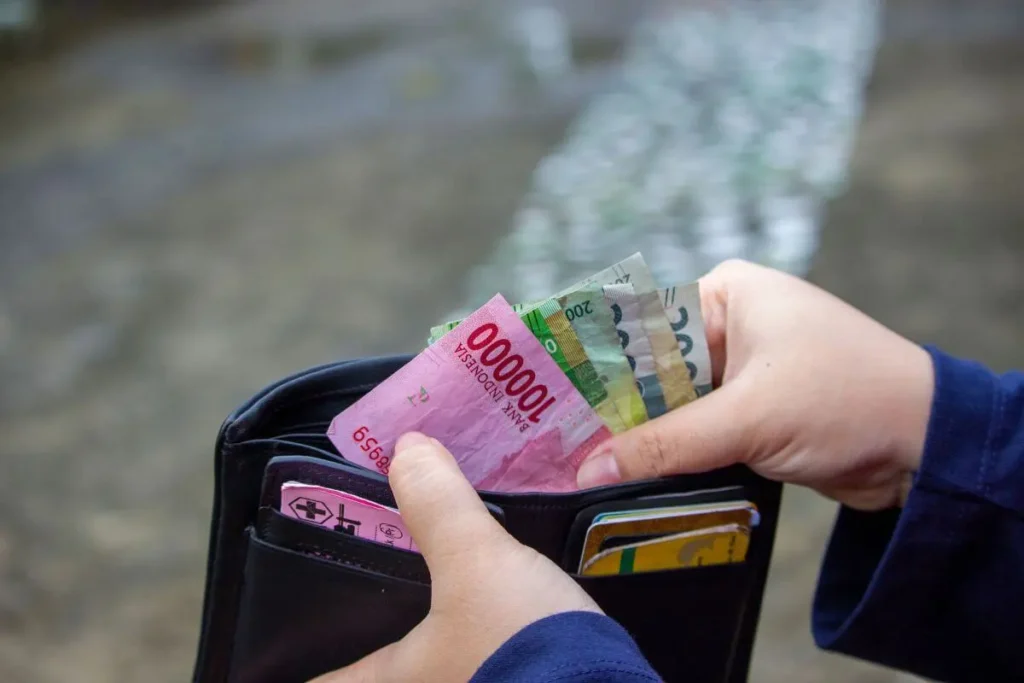 Pessoa segurando uma carteira aberta com cédulas de dinheiro e cartões.