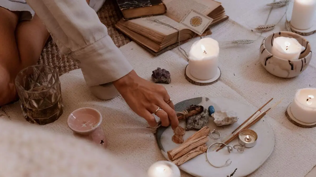 Pessoa preparando um ritual espiritual com velas acesas, cristais, incenso e ervas.
