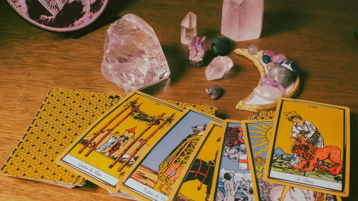Cartas de tarô abertas sobre uma mesa de madeira com cristais usados em leitura espiritual.