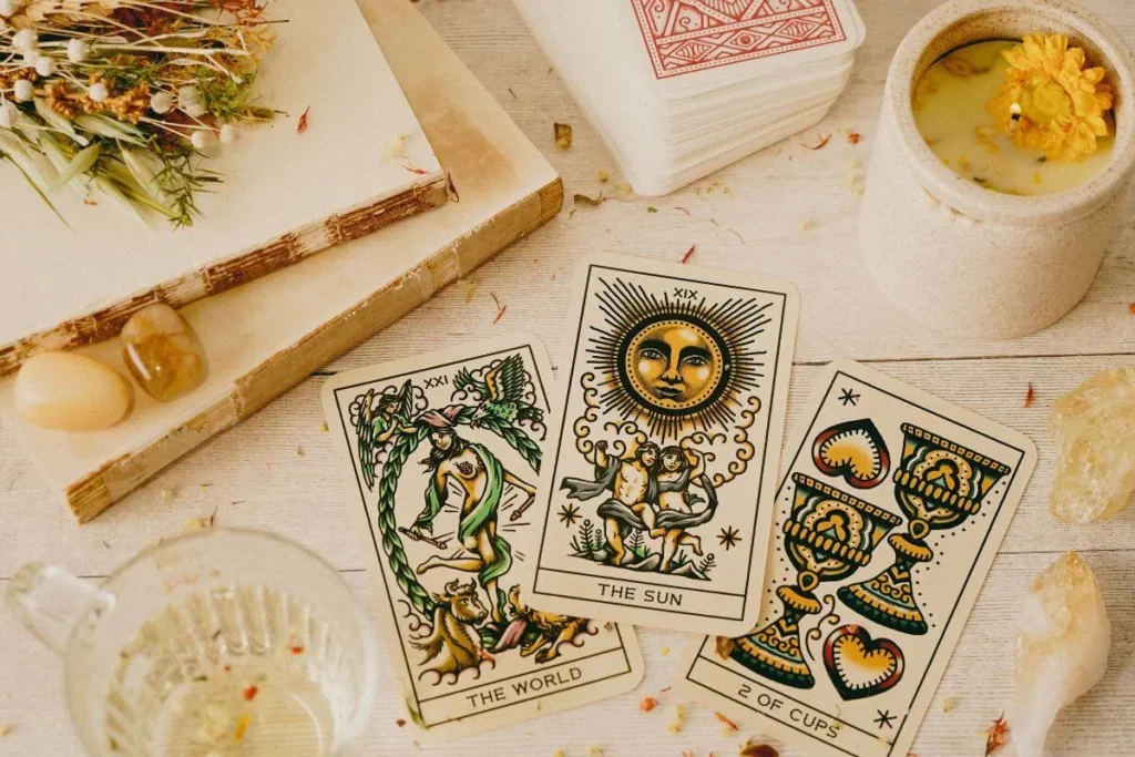 Cartas de tarô O Sol, O Mundo e Dois de Copas sobre uma mesa com cristais, flores secas e vela acesa.