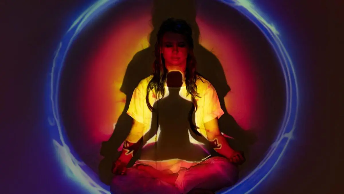 Mulher meditando em posição de lótus cercada por luzes coloridas que representam energia e equilíbrio espiritual.