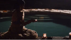 Mulher segurando uma pequena vela acesa durante ritual espiritual à beira da água.