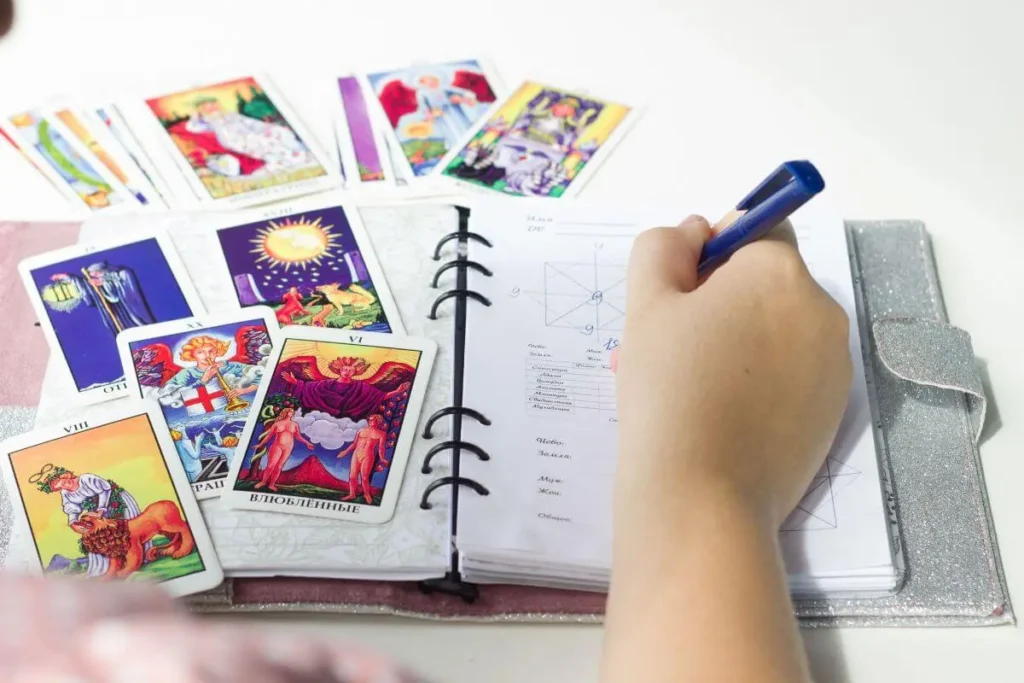 Caderno com perguntas abertas ao lado de cartas de Tarô