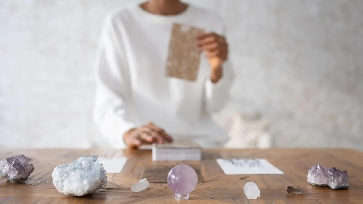 Pessoa realizando uma tiragem de tarô sobre mesa com cristais e esfera de ametista
